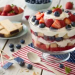 Layered Red, White & Blue Trifle with cream, strawberries, and blueberries in a glass bowl on a festive July 4th table.