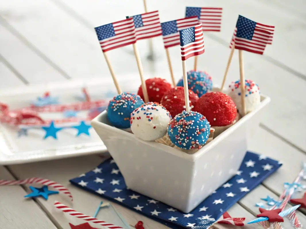 Red, white, and blue cake pops with patriotic sprinkles on sticks, arranged in a container for a 4th of July party dessert